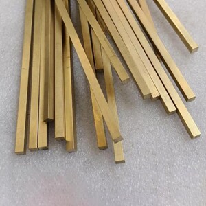 May include: A collection of rectangular brass bars, each with a golden hue. The bars are of varying lengths and are arranged in a scattered pattern. The metal bars are likely used for crafting or construction.