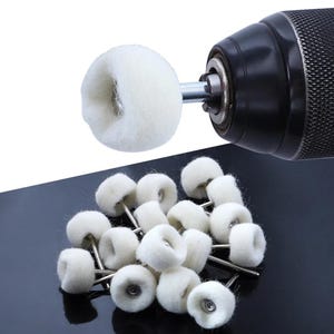 May include: A collection of white felt polishing wheels with metal stems, alongside a drill. The wheels are cylindrical and fluffy, designed for buffing and polishing various surfaces. The drill is black and silver.