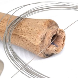 May include: A close-up of a wooden saw handle with a silver wire threaded through the hole. The wire is coiled around the handle.