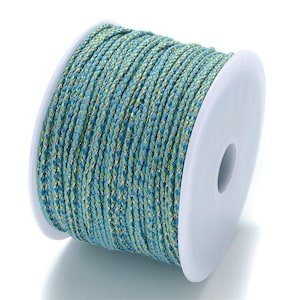 Puede incluir: Un carrete de cordón trenzado turquesa y dorado. El cordón está enrollado firmemente en una bobina de plástico blanco. El cordón tiene un aspecto texturizado con una mezcla de hilos azules, verdes y dorados. Ideal para la fabricación de joyas y manualidades.