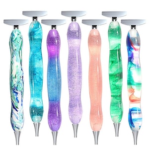 Peut inclure: Sept stylos de peinture diamant avec des pointes et des dessus argentés. Les stylos présentent une variété de motifs, notamment des tourbillons, des paillettes et des dégradés de couleurs dans des tons de bleu, vert, violet et rose.