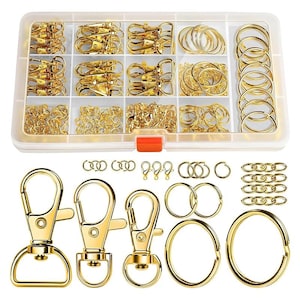 May include: A set of gold-coloured keychains and rings in a clear plastic storage box. The set includes various sizes of key rings, swivel clasps, and chain links.