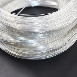 May include: A continuous coil of thin, reflective silver-colored wire wound into a circular shape. The metallic strands are smooth and uniform, creating a dense, layered bundle with a bright, polished appearance that catches the light.
