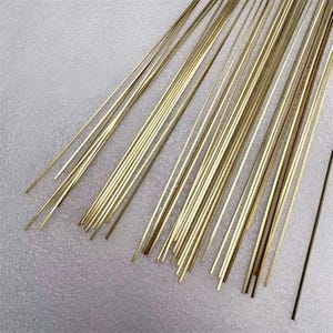 May include: A collection of thin, straight, golden-colored metal rods. The rods are arranged in a loose bundle, with a few isolated rods visible. The rods appear to be made of brass or a similar alloy, and are likely used in crafting or jewelry making.