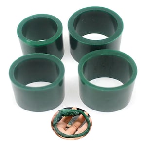 Puede incluir: Cuatro anillos de cera cilíndricos de color verde oscuro se muestran sobre un fondo blanco. Los anillos están espaciados uniformemente y tienen una superficie lisa y pulida. Una imagen circular más pequeña muestra una pulsera de cera verde.