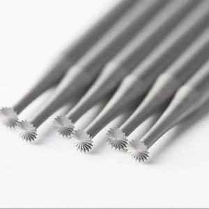May include: A collection of grey dental burrs, each featuring a star-shaped cutting head. The burrs are angled against a white backdrop, highlighting their intricate design and precision, suitable for dental work.