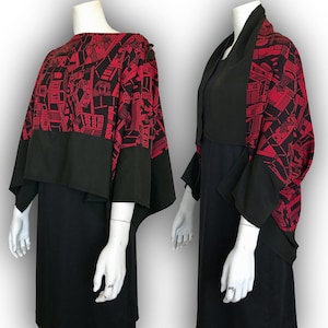 May include: A black dress with a red and black geometric print cape. The cape has a wide, flowing shape and is worn over the dress.