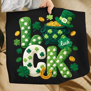 May include: Black textile featuring a St. Patrick's Day design with the word "LUCK" in green and white crochet. The design includes a pot of gold, a green hat, shamrocks, and gold coins. A horseshoe is also included.