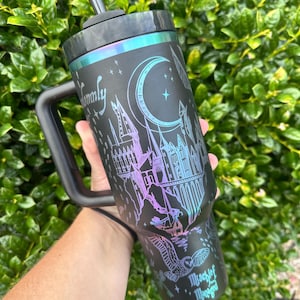 May include: Black tumbler with a handle, straw, and iridescent accents. The tumbler features a castle design, a crescent moon, stars, and the words "Mischief Managed" and "Family".