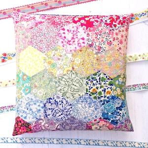 May include: A colourful patchwork cushion with a hexagonal pattern. The cushion is made of various floral fabrics in shades of pink, yellow, blue, green, and purple.