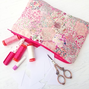 May include: A pink floral zippered pouch with a pink zipper pull, filled with sewing supplies including pink and white thread spools, a pink marker, a white glue stick, and a pair of silver scissors.