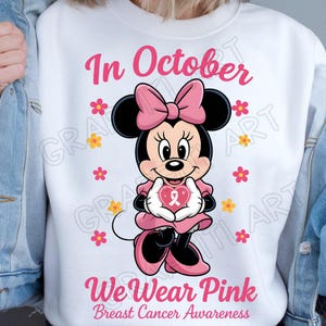 May include: White sweatshirt featuring Minnie Mouse holding a pink heart with a ribbon, surrounded by pink and yellow flowers. The text "In October" and "We Wear Pink Breast Cancer Awareness" are displayed in pink.