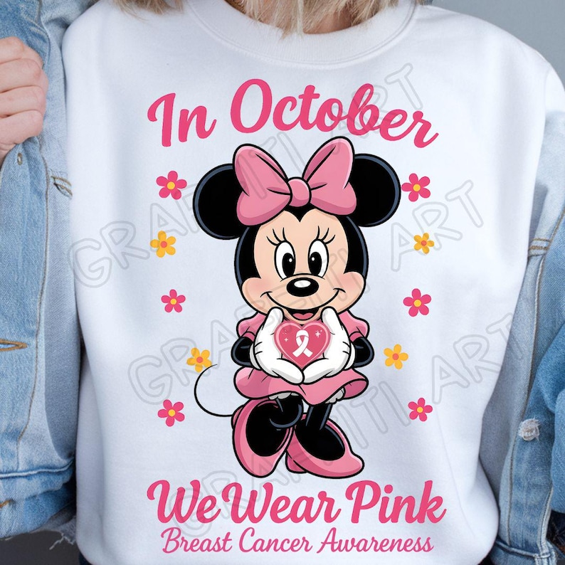 May include: White sweatshirt featuring Minnie Mouse holding a pink heart with a ribbon, surrounded by pink and yellow flowers. The text "In October" and "We Wear Pink Breast Cancer Awareness" are displayed in pink.