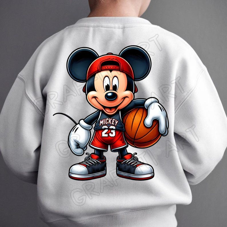 Peut inclure: Sweat-shirt blanc avec une image de dessin anim&eacute; de Mickey Mouse portant un maillot de basket-ball rouge avec le num&eacute;ro 23 et le mot "Mickey" dessus. Il tient un ballon de basket et porte une casquette de baseball rouge.