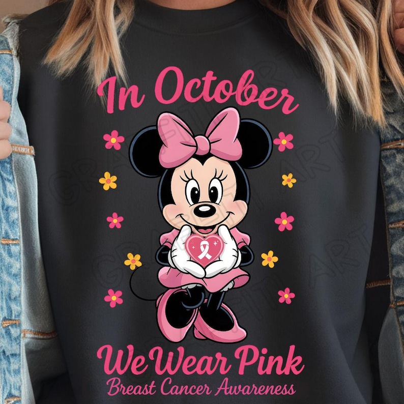 May include: Black sweatshirt featuring Minnie Mouse in pink attire, holding a pink heart with a ribbon. The text "In October We Wear Pink Breast Cancer Awareness" is displayed in pink.