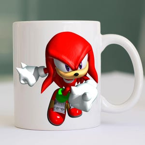 May include: White ceramic mug featuring a vibrant illustration of Knuckles the Echidna, a red echidna character with white gloves and red shoes. The mug has a white handle and is suitable for hot or cold beverages.