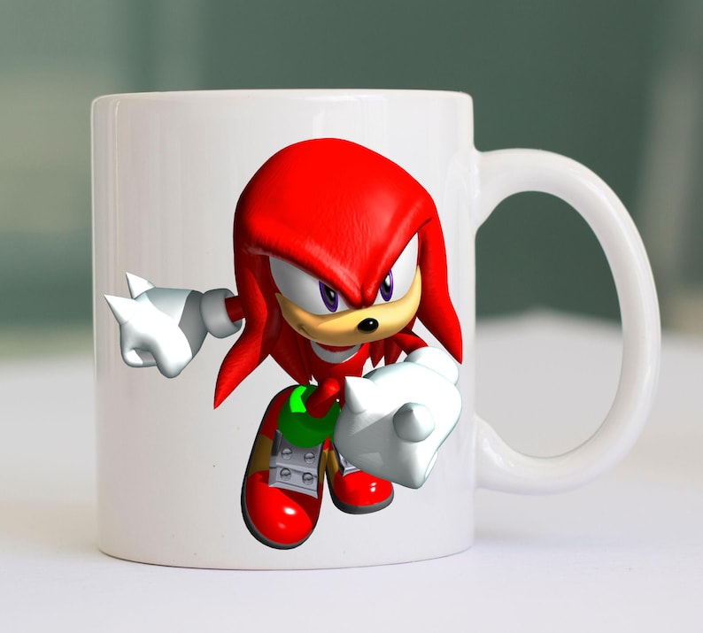 May include: White ceramic mug featuring a vibrant illustration of Knuckles the Echidna, a red echidna character with white gloves and red shoes. The mug has a white handle and is suitable for hot or cold beverages.