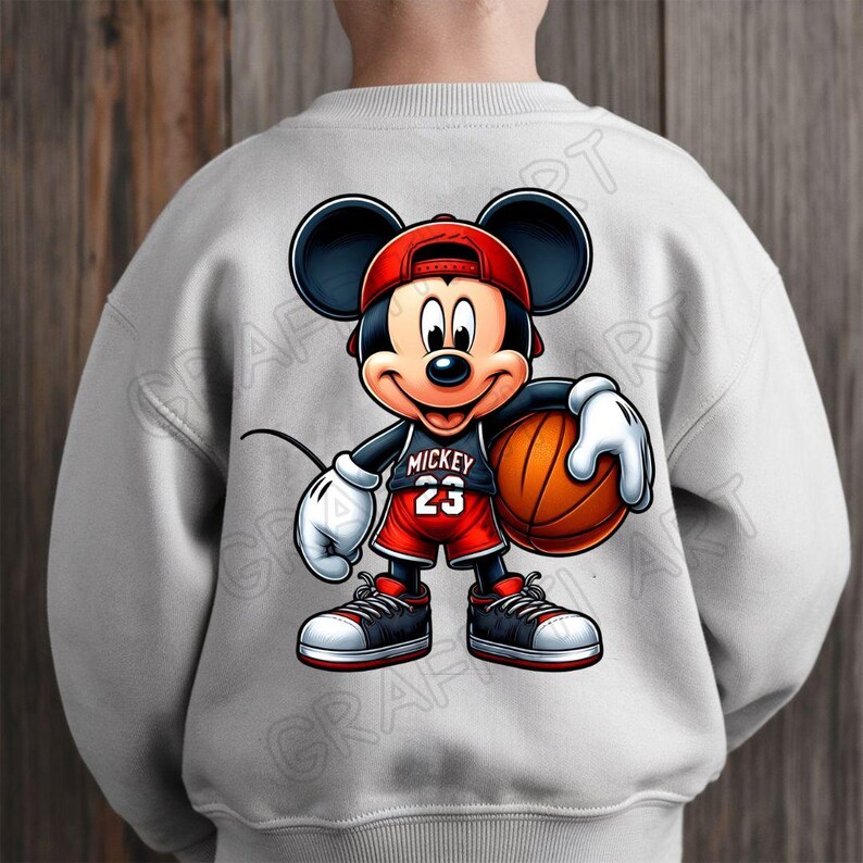 Peut inclure: Un sweat-shirt gris avec une image de dessin anim&eacute; de Mickey Mouse jouant au basket-ball. Mickey porte un maillot rouge et blanc avec le mot "Mickey" et le num&eacute;ro "23" dessus. Il tient un ballon de basket dans sa main droite.