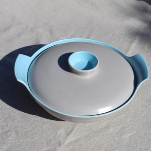May include: A grey ceramic serving bowl with a light blue rim and lid. The lid has a small, light blue knob in the centre.