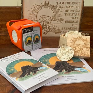 May include: An orange Yoto speaker and accompanying cards are displayed with books and wooden art pieces. The books and wooden art feature the title "The Shoot of Jesse" and artwork of a tree stump and sun.