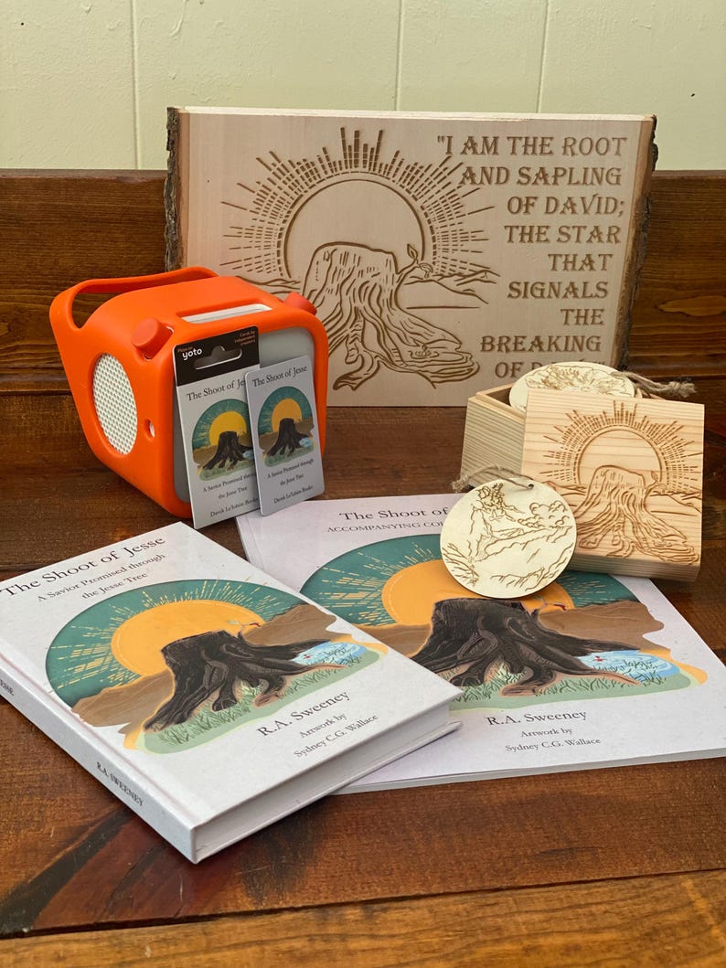 May include: An orange Yoto speaker and accompanying cards are displayed with books and wooden art pieces. The books and wooden art feature the title "The Shoot of Jesse" and artwork of a tree stump and sun.