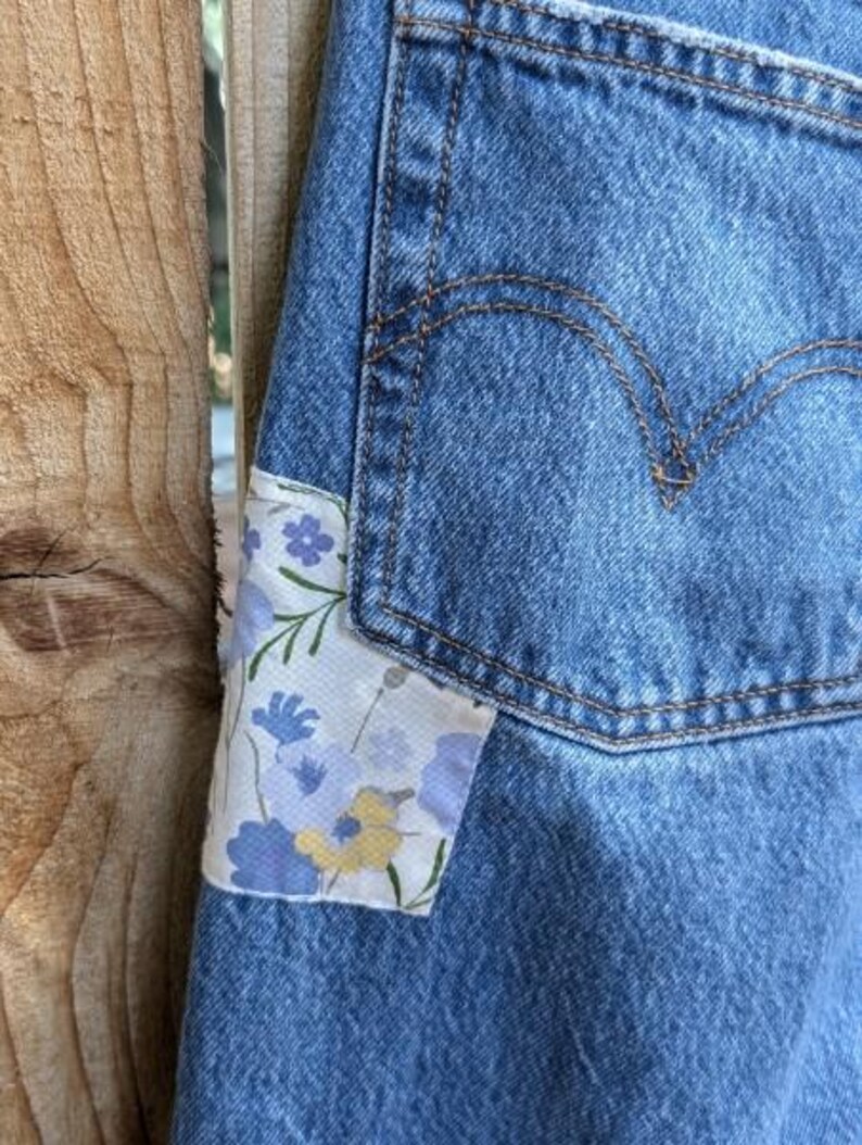 Pu&ograve; includere: Jeans blu denim con una toppa floreale cucita sulla tasca anteriore.