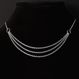 Może przedstawiać: Srebrny naszyjnik z łańcuszkiem o trzech rzędach i dwoma okrągłymi zapięciami.