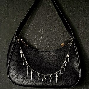 May include: Black leather handbag with a silver chain strap adorned with charms, including crescent moons, stars, and swords.