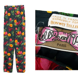 Puede incluir: Pantalones negros con estampado floral con flores rojas, amarillas y naranjas. Los pantalones est&aacute;n colgados de una percha blanca. La etiqueta dice "Made in France expressly for Bonwit Teller" y "Willy van Rooy Paris."
