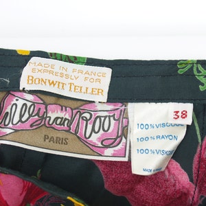 Puede incluir: Primer plano de una tela oscura con estampado floral con varias etiquetas. Las etiquetas dicen "MADE IN FRANCE EXPRESSLY FOR BONWIT TELLER" y "Willy van Rooy PARIS". La tela tiene un patr&oacute;n de grandes flores rosas y hojas verdes.