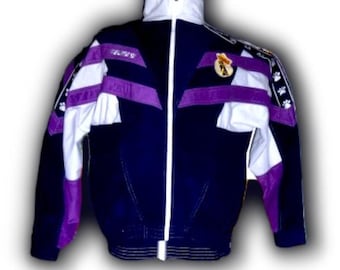 May include: A vintage navy blue track jacket with white and purple accents. The jacket features a white zipper, a high collar, and a crest on the chest. The sleeves have white and purple panels with paw print details.