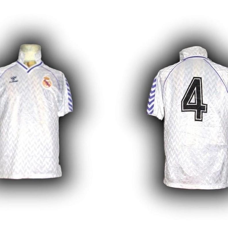 Puede incluir: Camiseta de f&uacute;tbol blanca con un patr&oacute;n texturizado, detalles azules y el n&uacute;mero 4 en la espalda. La camiseta tiene cuello y un logo del equipo. Las mangas tienen rayas azules y blancas.