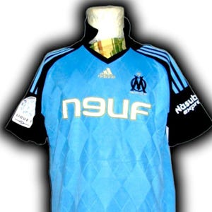 Puede incluir: Camiseta de f&uacute;tbol azul claro con mangas y detalles en negro. La camiseta presenta el logo de Adidas, el emblema del equipo de Marsella y la palabra "NEUF" en letras doradas. Las mangas tienen rayas azules y la camiseta tiene un patr&oacute;n de diamantes.