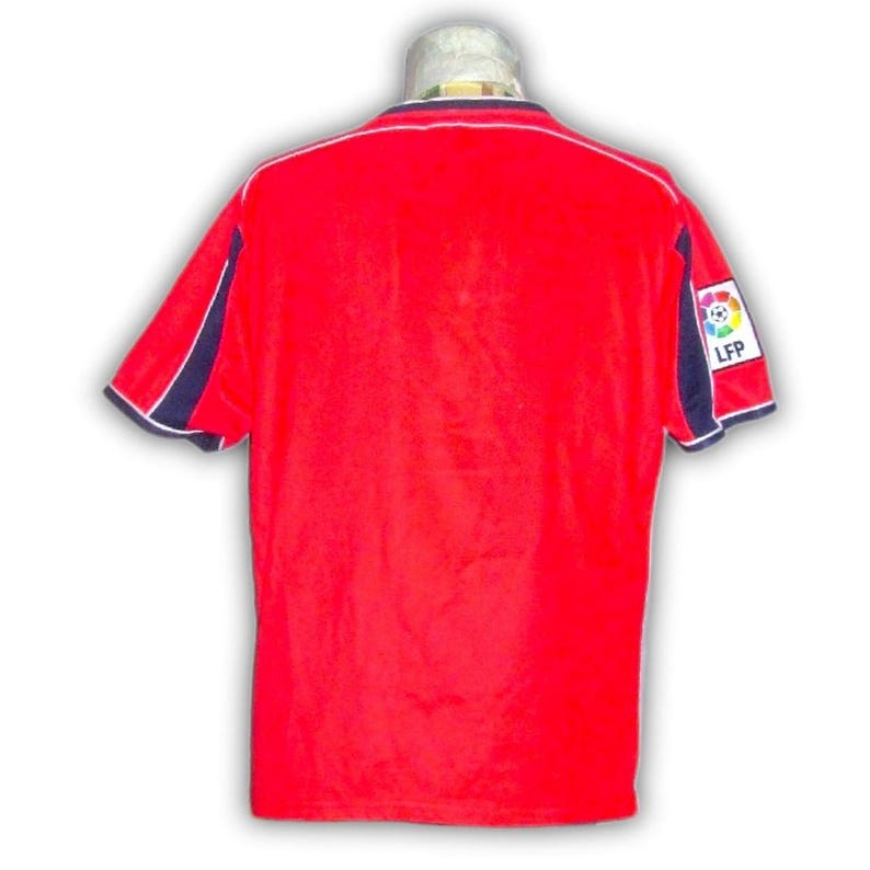 K&ouml;nnte beinhalten: Ein rotes Fu&szlig;balltrikot mit marineblauen und wei&szlig;en Akzenten. Das Trikot hat kurze &Auml;rmel und einen wei&szlig;en Kragen. Ein Aufn&auml;her mit einem Fu&szlig;ball und den Buchstaben "LFP" befindet sich auf dem rechten &Auml;rmel.