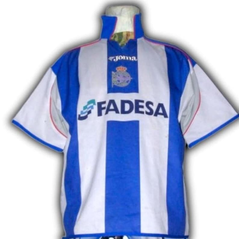 May include: A white and blue soccer jersey with vertical blue stripes and white sleeves. The jersey features the "Joma" logo, a team emblem, and the "FADESA" sponsor logo. The jersey has a high collar and short sleeves.