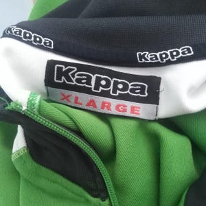 K&ouml;nnte beinhalten: Gr&uuml;n-schwarze Kappa XLARGE-Jacke mit Rei&szlig;verschluss. Die Jacke hat einen wei&szlig;en Kragen mit dem Kappa-Logo in Wei&szlig;. Das XLARGE-Etikett ist auf der Vorderseite sichtbar. Der Rei&szlig;verschluss ist schwarz, und die Jacke ist aus weichem, strukturiertem Material.