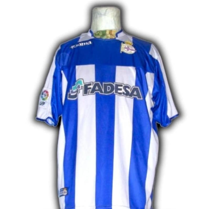 May include: A blue and white striped soccer jersey with the word "FADESA" across the front. The jersey has short sleeves and a round collar. Logos are visible on the sleeves and chest.