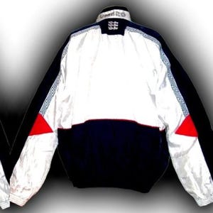 May include: A vintage Umbro England soccer jacket. The jacket features a white upper section, a navy blue lower section, and black sleeves. Red triangles accent the sides. The Umbro logo and England crest are visible on the collar.