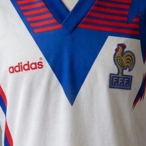 May include: White Adidas soccer jersey with blue and red accents. Features a blue V-neck collar with red stripes and the Adidas logo in red. The French Football Federation emblem is on the chest.