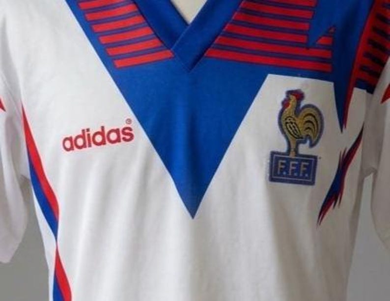 May include: White Adidas soccer jersey with blue and red accents. Features a blue V-neck collar with red stripes and the Adidas logo in red. The French Football Federation emblem is on the chest.
