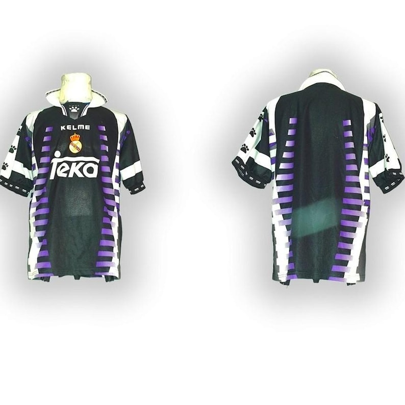 May include: Black and purple soccer jersey with white accents. The jersey features the Kelme logo, a crest, and the Teka sponsor logo. The sleeves have paw print designs. The back of the jersey has vertical purple stripes.