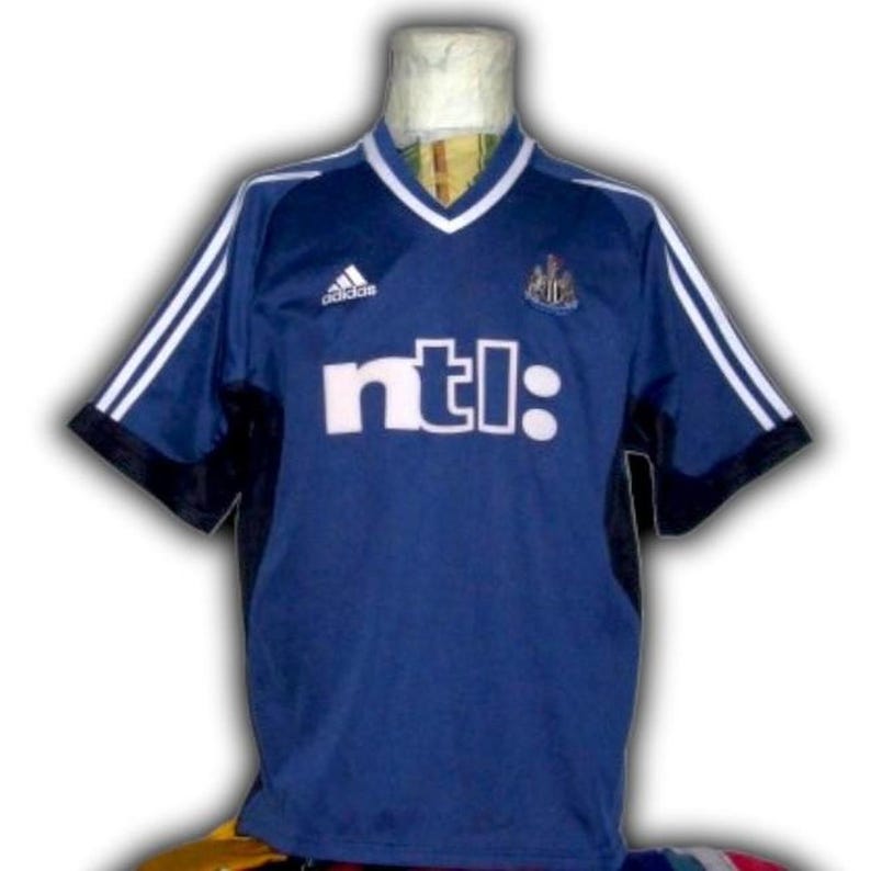 May include: A navy blue soccer jersey with white accents and the text "ntl:" across the front. The jersey features white stripes on the sleeves, a white V-neck collar, and the Adidas logo.