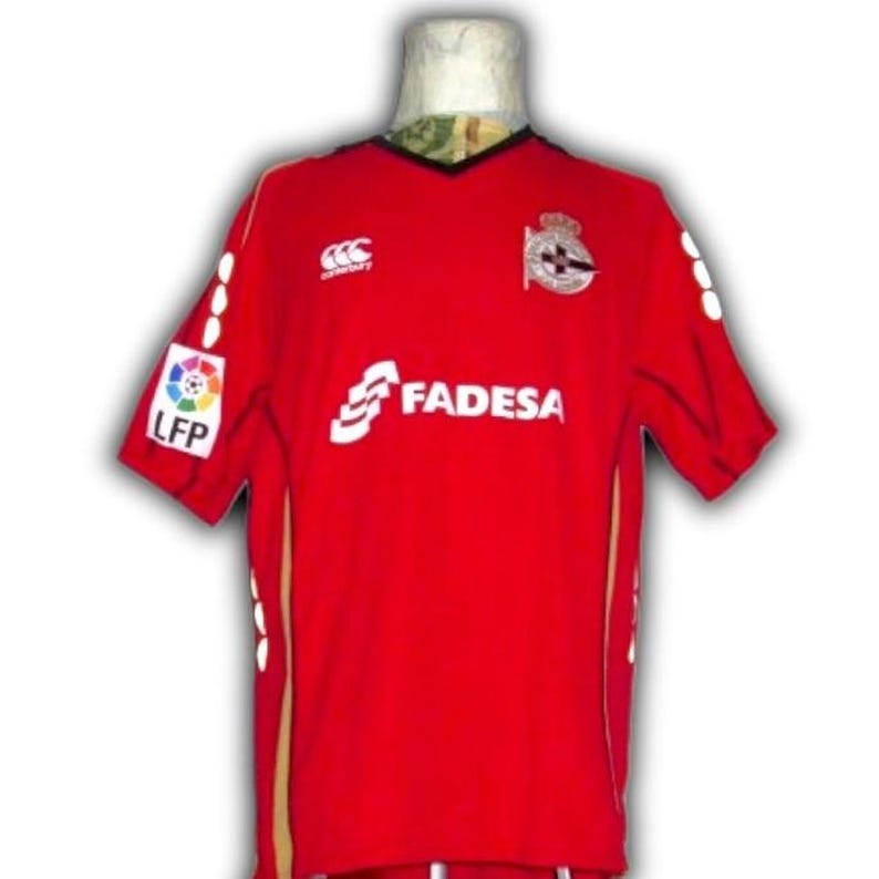 May include: A red soccer jersey with white logos and text, including "FADESA" and "LFP." The jersey has a black collar and gold accents. The Canterbury logo is visible on the chest.