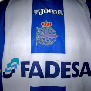 May include: A blue and white soccer jersey with the "Joma" logo at the top. The jersey features the Real Club Deportivo La Coru&ntilde;a crest and the "FADESA" sponsor logo.