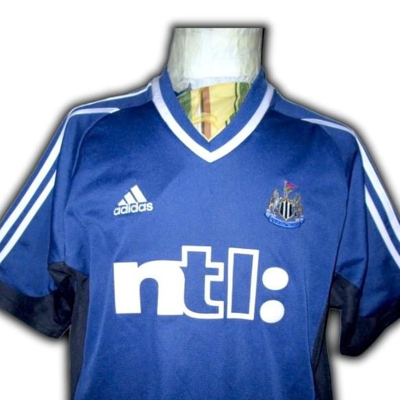 May include: Blue soccer jersey with white stripes on the shoulders and sleeves. Features the Adidas logo, a team crest, and the word "ntl:" in white block letters. The jersey has a V-neck collar with white trim.