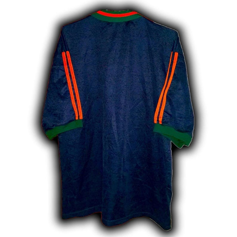 May include: Navy blue jersey with orange stripes on the sleeves and a green collar and sleeve cuffs. The jersey has a textured pattern and a crew neck with orange and green trim.