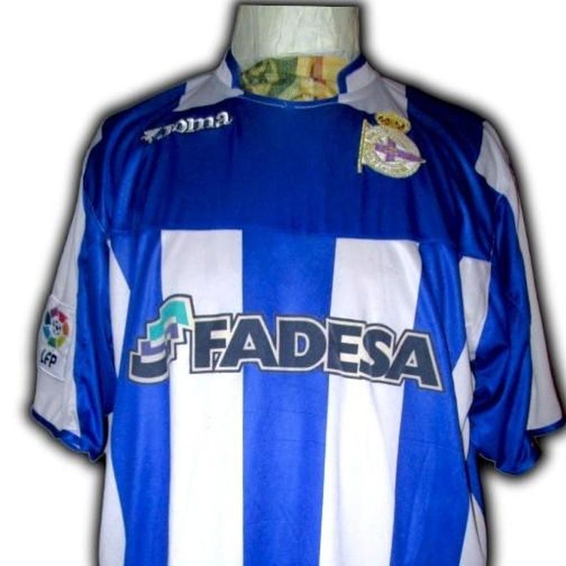 May include: A blue and white striped soccer jersey with the word "FADESA" across the front. The jersey has a blue collar and sleeves, with the "Joma" logo on the upper chest. A team emblem is on the right chest.