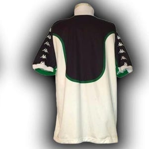 Op de afbeelding: Een wit en zwart shirt met groene rand. Het shirt heeft een zwart bovenpaneel op de rug en groene accenten. De mouwen zijn zwart met witte logo's. De kraag is wit. Dit shirt is waarschijnlijk voor een sportteam.