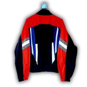 Puede incluir: Chaqueta deportiva vintage en negro, rojo y azul. La chaqueta tiene cuello alto, cremallera completa y patrones geom&eacute;tricos en las mangas. Las mangas son negras con detalles en rojo y blanco. La espalda es negra con rayas azules y blancas.