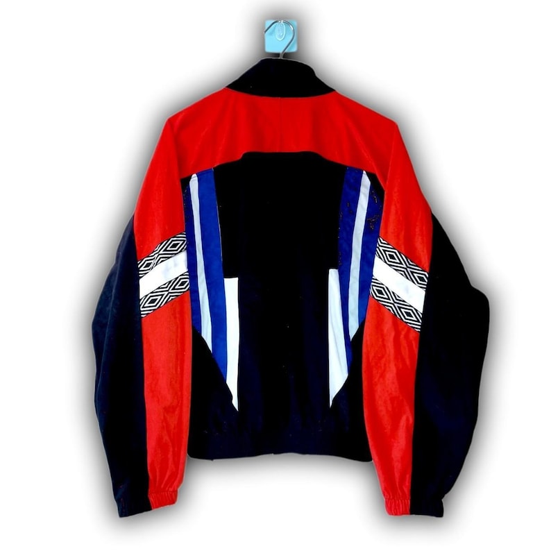 Puede incluir: Chaqueta deportiva vintage en negro, rojo y azul. La chaqueta tiene cuello alto, cremallera completa y patrones geom&eacute;tricos en las mangas. Las mangas son negras con detalles en rojo y blanco. La espalda es negra con rayas azules y blancas.